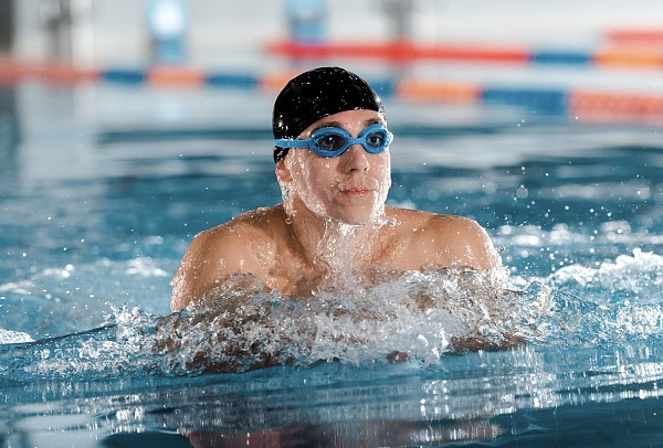 Mann mit schwarzer Badekappe und Schwimmbrille beim Luftholen an der Wasseroberfläche