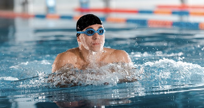 Mann mit schwarzer Badekappe und Schwimmbrille beim Luftholen an der Wasseroberfläche